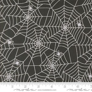 May include: Black fabric with a white spiderweb pattern and small spiders. The fabric has a repeating design of spiderwebs and spiders, perfect for Halloween or spooky-themed crafts. The fabric is marked with a ruler along the bottom.