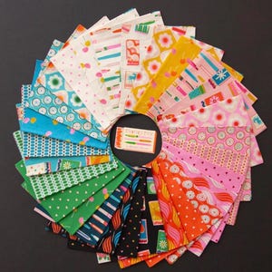 May include: A circular arrangement of colorful fabric squares with various patterns, including flowers, cherries, and geometric designs. The fabrics are in shades of pink, yellow, blue, and green. A small card in the center reads "Tranketry".