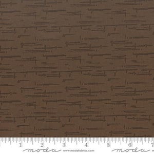 May include: A brown fabric featuring a repeating pattern of dark brown horizontal lines and small dashes. A white ruler is visible at the bottom edge, showing measurements in inches from 0 to 7 inches, with the text moda and modafabrics.com.