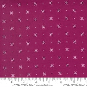May include: A pink fabric with a white repeating pattern of small crosses. The fabric has a subtle texture and is marked with "moda" and a website address.