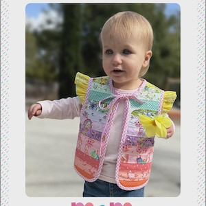 May include: A baby-sized reversible patchwork vest with a colorful design. The vest features a variety of fabric patterns in shades of pink, purple, green, and yellow. The vest has a pink trim and yellow ruffled sleeves. The text "HARMONY VEST" is at the top.