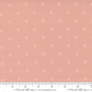 May include: Peach-colored fabric with a repeating pattern of small, white cross-like shapes. The fabric has a textured appearance and a ruler is visible along the bottom edge, marked in inches.