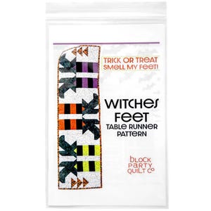 May include: A Halloween-themed table runner pattern titled "Witches Feet." The design features a colorful patchwork pattern with black, orange, purple, and yellow blocks. The text "Trick or Treat Smell My Feet!" is also visible.