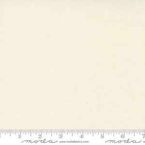 May include: A solid off-white fabric with a subtle texture. The fabric is shown with a ruler for scale.
