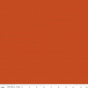 May include: Close-up of a textured orange fabric with a small dot pattern. The fabric is measured in inches, with a ruler along the bottom edge. The fabric is from Riley Blake Designs.
