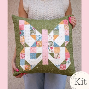 May include: A green quilted pillow with a butterfly design made of patchwork squares in various colors and floral patterns. The butterfly has a pink center and white wings. The pillow is held by a person. The word "Kit" is in the lower right corner.