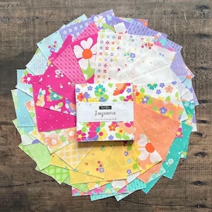 May include: A stack of square fabric swatches arranged in a circular fan pattern. The fabric features various floral, polka dot, and checkered prints in pink, yellow, orange, green, and blue. A white paper band labeled Joysome wraps the center.