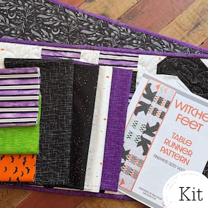 May include: A quilting kit featuring a table runner pattern titled Witch Feet, finished size 14x50 inches, alongside various fabric swatches in black, white, purple, green, and orange, featuring patterns of bats, stars, and stripes.
