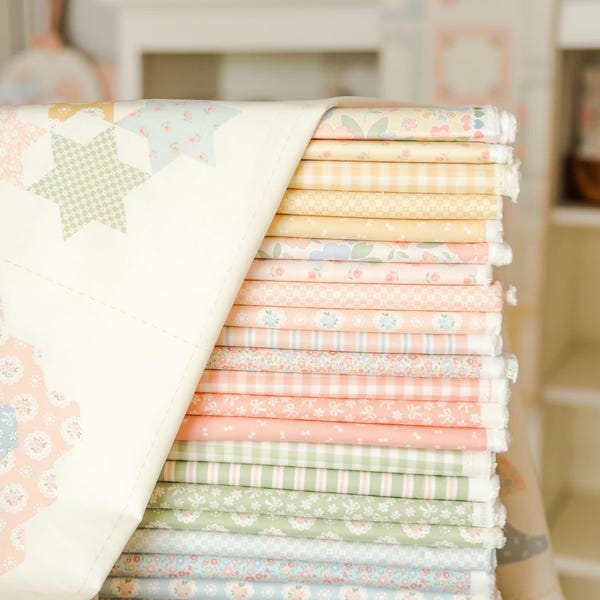 May include: A tall stack of folded fabric squares in a variety of pastel colors including yellow, peach, green, and blue. The fabrics feature patterns such as gingham, floral prints, and small geometric shapes, with a quilt draped over the side.
