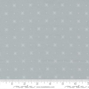 May include: A light blue fabric with a repeating pattern of white cross-stitch designs. The fabric has a textured appearance and a ruler is at the bottom, with measurements in inches.