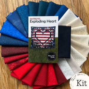 May include: A quilt kit featuring a pattern booklet titled Patriotic Exploding Heart by Slice of Pi Quilts, surrounded by a fan of folded fabric swatches in shades of red, white, navy blue, and dark teal with various subtle tonal patterns.