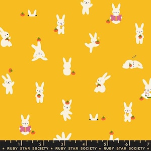 May include: A mustard yellow fabric featuring a repeating pattern of small white rabbits in various poses, including reading, sleeping, and holding red tomatoes. A black ruler at the bottom shows measurements from 1 to 7 inches.