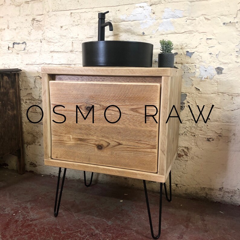 K&ouml;nnte beinhalten: Ein rustikaler Badezimmer-Waschtisch aus Holz mit einem schwarzen Keramikwaschbecken und einem Einhebelmischer. Der Waschtisch hat eine Schublade und steht auf Haarnadelbeinen. Der Text "OSMO RAW" ist auf der Vorderseite des Waschtisches sichtbar.