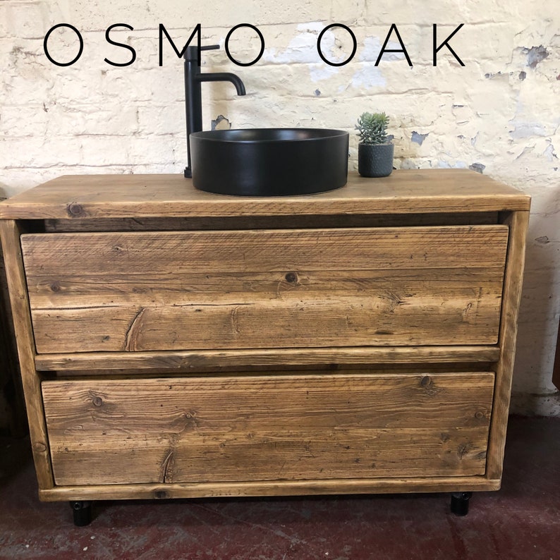 K&ouml;nnte beinhalten: Ein rustikaler Badezimmer-Waschtisch aus Holz mit zwei Schubladen und einem schwarzen runden Waschbecken. Der Waschtisch hat einen schwarzen Wasserhahn und ist mit "OSMO OAK" beschriftet.