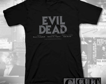 May include: Black V-neck t-shirt featuring the text "EVIL DEAD" in grey block letters. The names Bruce Campbell, Robert G. Tapert, and Sam Raimi are printed below. The shirt also has a "CULT RATED" logo.