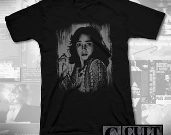 May include: Black V-neck t-shirt with a grayscale portrait of a woman with a startled expression. The image has a textured backdrop. The text "CULT RATED" is in the lower right corner of the shirt.