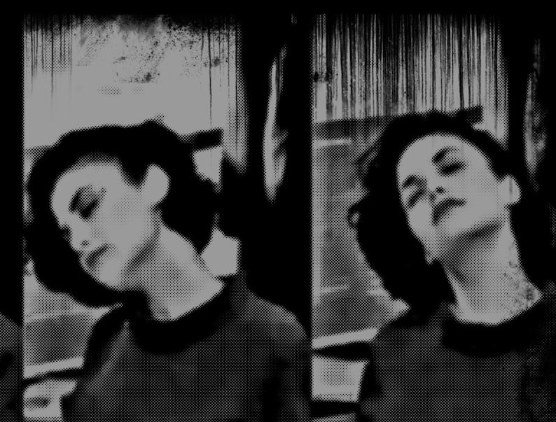 May include: Two women with dark hair and dark clothing pose for a black and white portrait. The women are looking down and their faces are partially obscured by shadows.