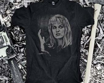 May include: Black t-shirt featuring a graphic print of a woman's face. The woman has long, dark hair and is wearing a white shirt. The background is a blurred image of a forest.