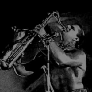 May include: A black and white photo of a person playing a saxophone. The person is shirtless and has their hair pulled back. The saxophone is held in a horizontal position.