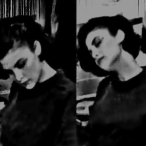 May include: Two women with short dark hair, wearing black shirts, are looking down. The image is in black and white.