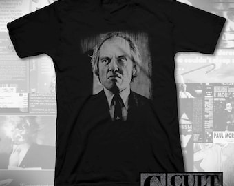 May include: Black V-neck t-shirt with a monochrome portrait of a man in a suit and tie. The image is a close-up of the man's face. The text "CULT RATED" is in the lower right corner.
