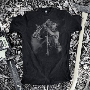 May include: Black t-shirt with a graphic print of a person playing a saxophone. The graphic is in shades of gray and the t-shirt is made of a soft, comfortable material.