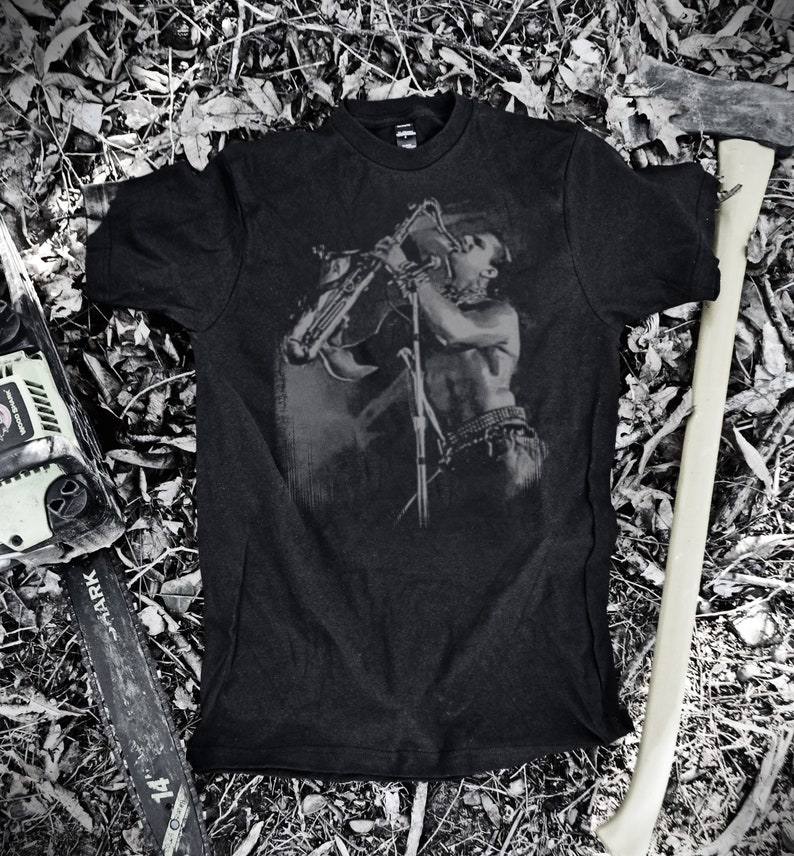 May include: Black t-shirt with a graphic print of a person playing a saxophone. The graphic is in shades of gray and the t-shirt is made of a soft, comfortable material.