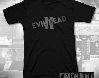 May include: Black V-neck t-shirt with the text "EVIL DEAD II" in grey, angled lettering. The shirt has a Cult Rated logo in the bottom right corner. The background features movie posters and text.