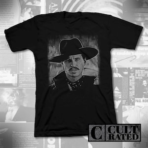 May include: Black t-shirt with a white graphic print of a man wearing a black cowboy hat and a black coat. The text "CULT RATED" is printed on a black rectangle at the bottom of the image.