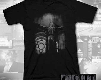 May include: Black V-neck t-shirt with a grayscale image of a figure with outstretched arms, set against a building with a stained-glass window. The text "CULT RATED" is in the lower right corner.