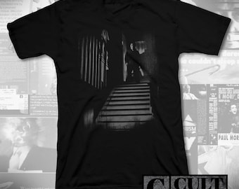 May include: Black V-neck t-shirt with a grayscale image of a person on a staircase in a dark hallway. The text "CULT RATED" is printed at the bottom right. The image has a film noir aesthetic.
