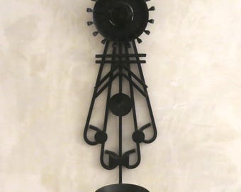 Peut inclure: Porte-bougie mural en métal noir avec un design géométrique. Le porte-bougie a un dessus circulaire avec un cercle plus petit au centre et une série de formes en goutte d'eau en cascade en dessous. Le bas du porte-bougie a un seul gobelet à bougie.
