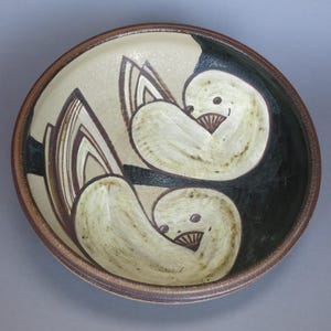 Könnte beinhalten: Eine Keramikschale mit braunem Rand und weißem Überzug. Die Schale zeigt ein stilisiertes Design von zwei Vögeln in Schwarz und Weiß.