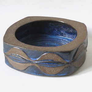 May include: A blue and brown ceramic bowl with a wavy design around the rim. The bowl is glazed and has a glossy finish.