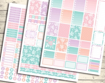 May include: A set of printable planner stickers with a floral design in shades of pink, purple, and green. The stickers include boxes, hearts, and other shapes. The text "Planner Stickers" is at the top of the page.