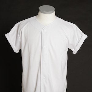 Könnte beinhalten: Weißes Baseballtrikot mit Knopfleiste und kurzen Ärmeln. Das Trikot hat ein kleines schwarzes gesticktes Logo mit der Aufschrift "dareville" unten rechts.