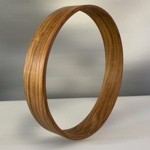 May include: A wooden hoop with a natural brown finish. The hoop is made of thin strips of wood that are glued together to create a circular shape.