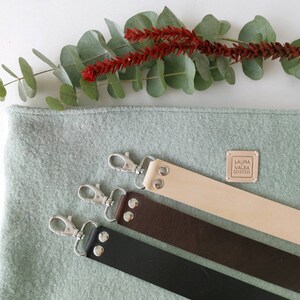 May include: Three leather straps with silver clasps and metal studs. The straps are beige, brown, and black. A small square label with the text "LAURA VALEA HANDMADE" is visible on the beige strap.