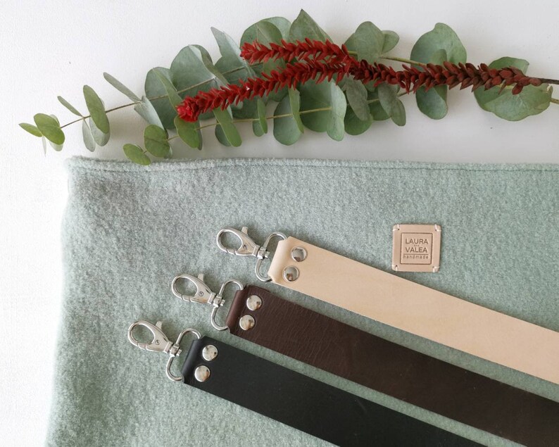 May include: Three leather straps with silver clasps and metal studs. The straps are beige, brown, and black. A small square label with the text "LAURA VALEA HANDMADE" is visible on the beige strap.