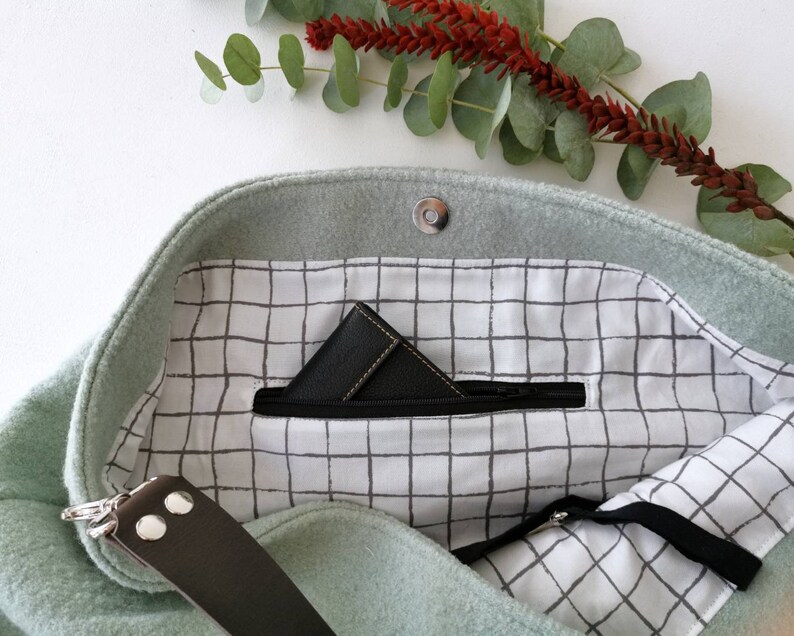 May include: A light green felt tote bag with a zippered pocket and a black and white grid pattern lining. The bag has a brown leather strap.