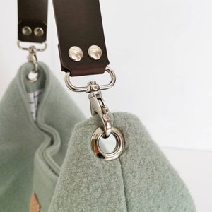 May include: A light green fabric bag with a brown leather strap and silver metal hardware. The strap has two silver metal rivets.