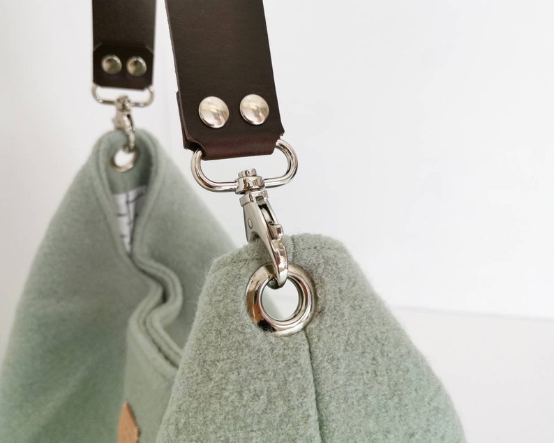 May include: A light green fabric bag with a brown leather strap and silver metal hardware. The strap has two silver metal rivets.