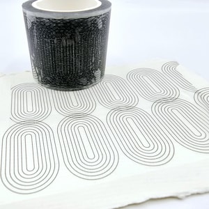 May include: A roll of black and white patterned washi tape with a geometric design. The tape is unrolled on a white surface, showing the pattern.