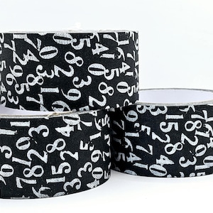 May include: Three rolls of black and white patterned washi tape with white numbers printed on a black background.