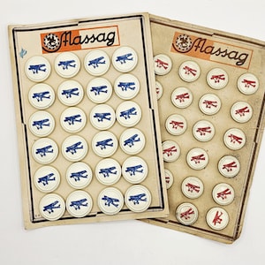 May include: Two vintage Massag game boards. One board features white circular game pieces with blue airplane designs, while the other has red airplane designs. The boards have a cream-colored background and the word "Massag" is printed at the top.