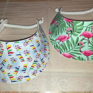 May include: Two sun visors with white rope headbands. The left visor features a light blue background with a pattern of colorful pennant flags and life preservers. The right visor has a light green background with a pattern of pink flamingos and green palm leaves.