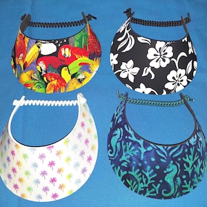 May include: Four sun visors with coil headbands. Top left features a colorful parrot and toucan print. Top right has a black background with white hibiscus flowers. Bottom left is white with small rainbow palm trees. Bottom right shows a blue sea life pattern.
