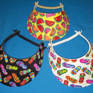 May include: Three sun visors with different patterns. One visor has a watermelon pattern on a yellow background. The other two visors have a flip-flop pattern on a black and white background.