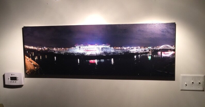 May include: A panoramic nighttime photograph of a city skyline with a large stadium lit up in the distance. The stadium is reflected in the water below. The city lights are visible in the background.