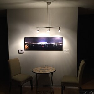 May include: Two chairs with a small round table in between them. The table has a mosaic tile top. The chairs are a light green color. A picture of a city skyline hangs on the wall above the table. A light fixture hangs from the ceiling.